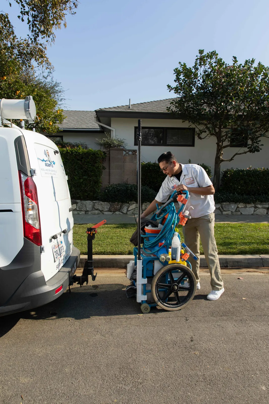 Adult and child loading a blue bicycle into the side door of a white van parked on a residential street.