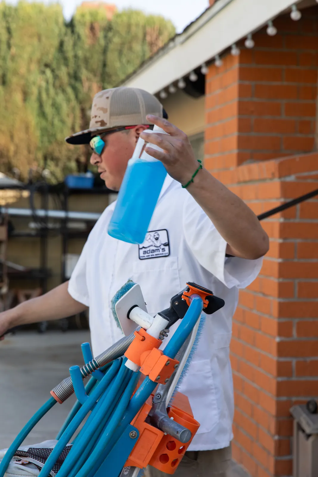 Person in white shirt and cap holding blue water bottle next to blue bicycle against red brick wall.