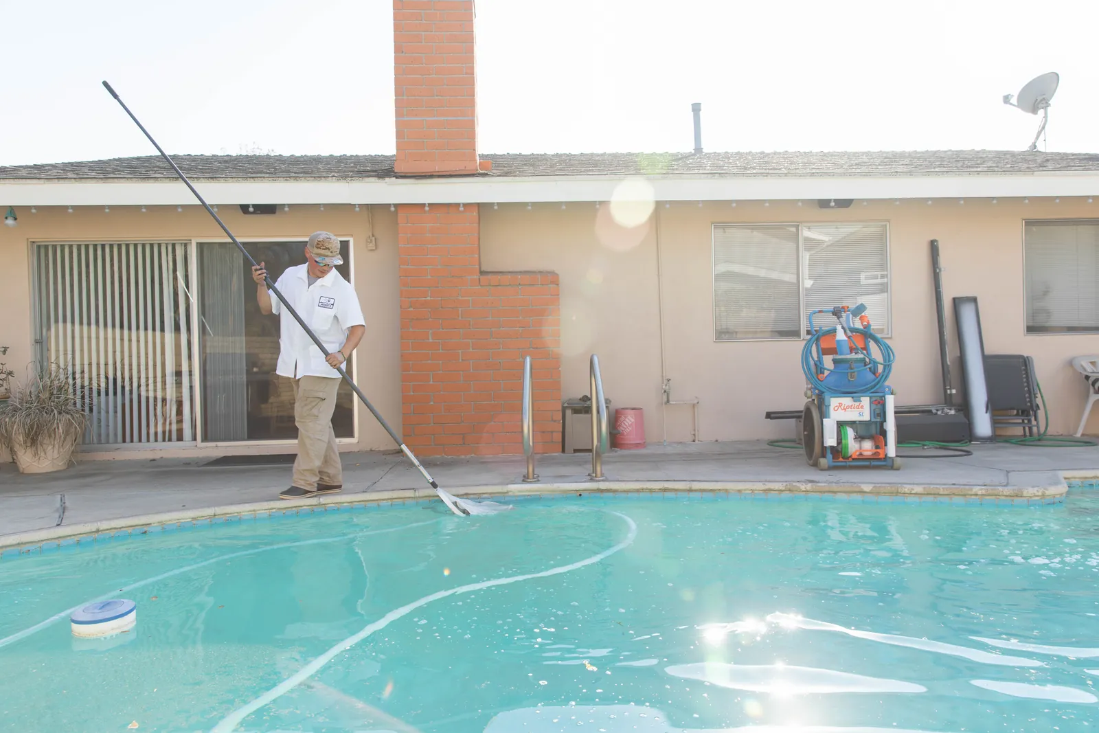 Person standing on pool deck using long-handled net to clean water in rectangular pool.