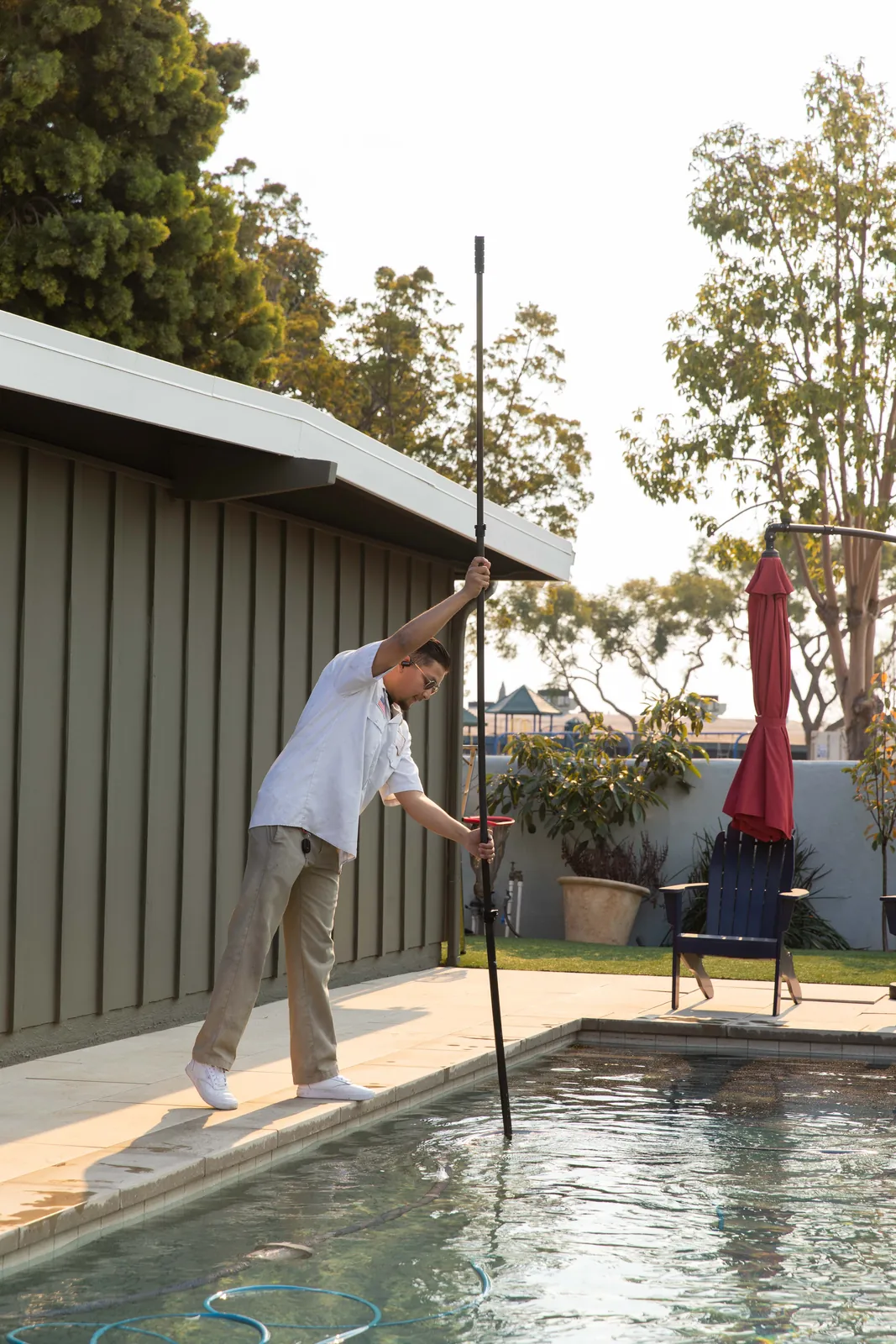 Person using pool skimmer net to clean water surface in residential backyard.