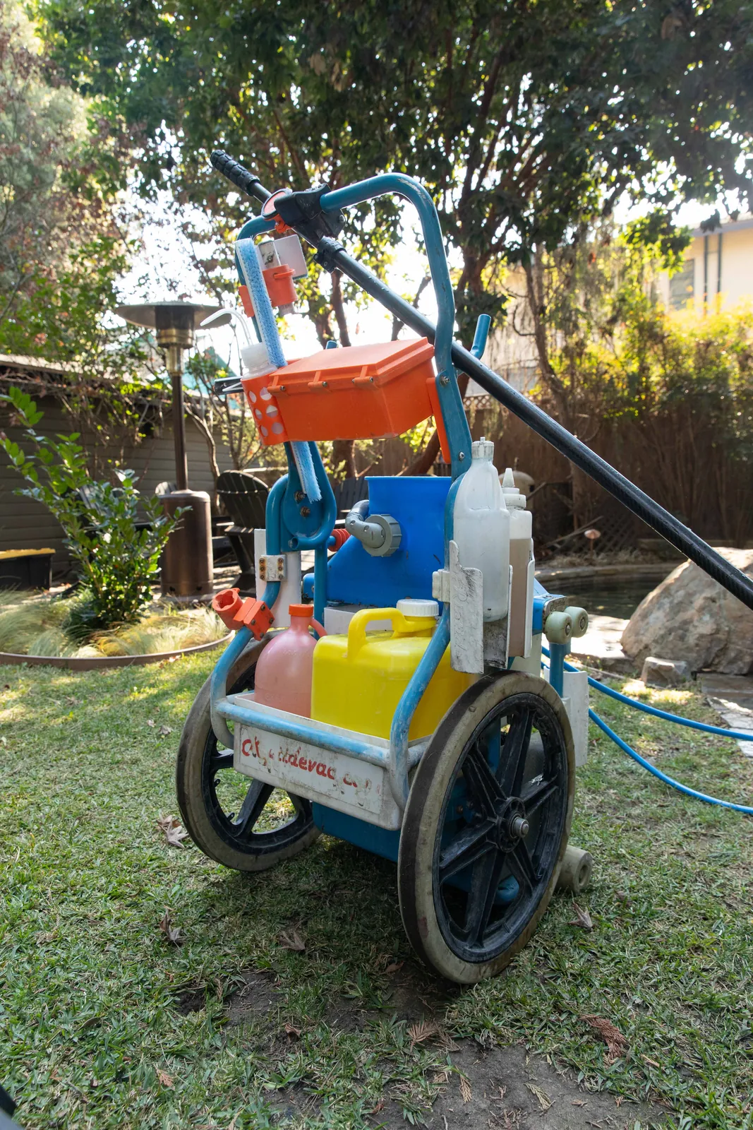 Portable pressure washer on wheels with orange tank and blue pump motor parked on grass.