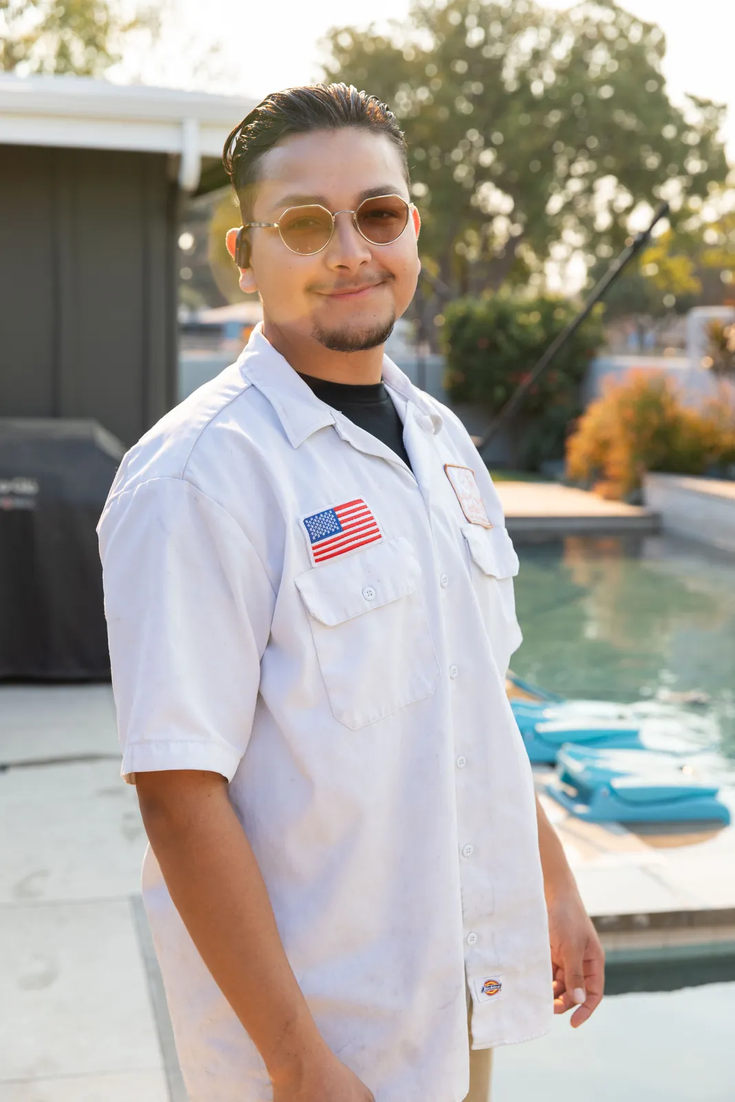 Man in white short-sleeve work shirt standing beside an outdoor swimming pool.