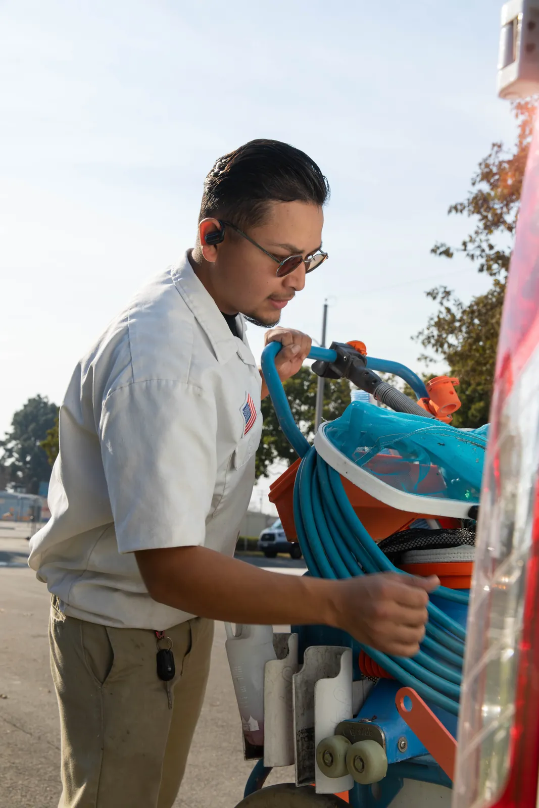 Person wearing glasses and light-colored shirt working on blue mechanical equipment mounted on exterior surface.