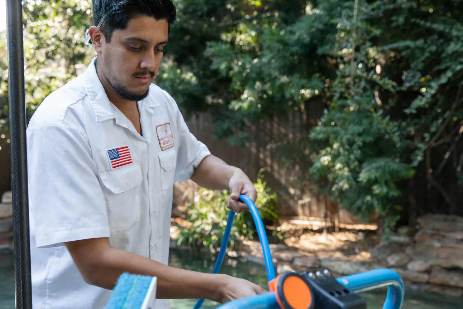 Person in white shirt working with blue equipment in an outdoor garden setting.