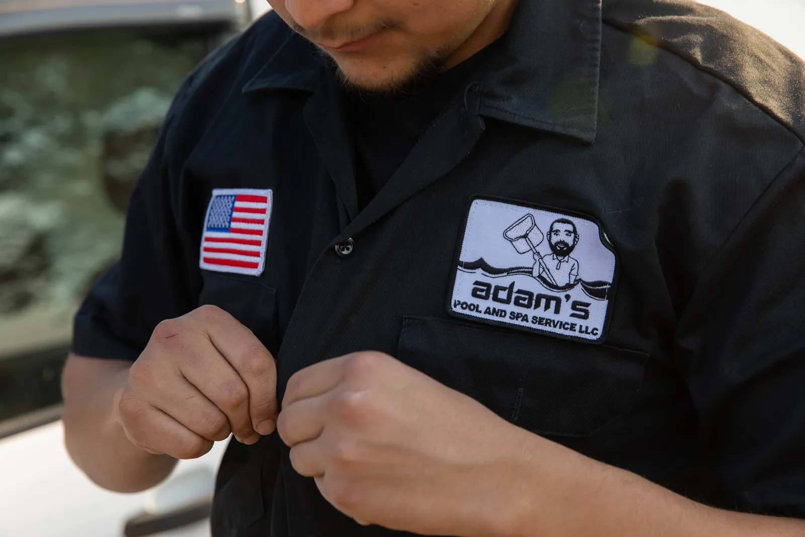 Person wearing dark uniform shirt with flag patch, hands demonstrating fastening action.